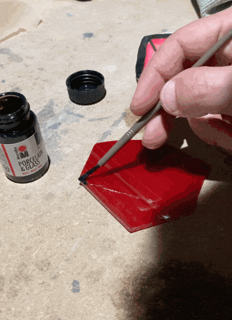 a gif of someone painting red glass with black paint