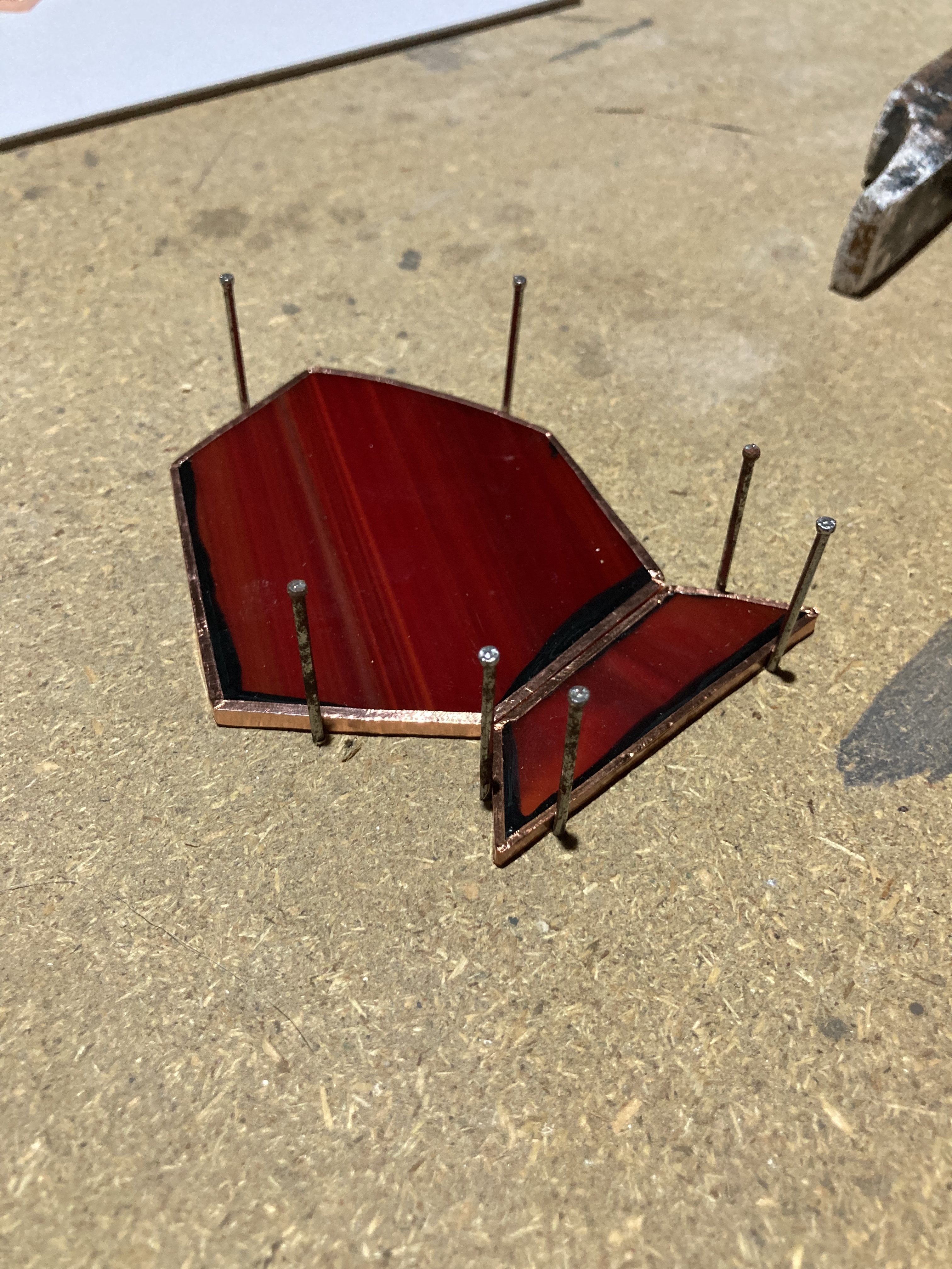 two foiled pieces of red glass held together by nails on a workbench
