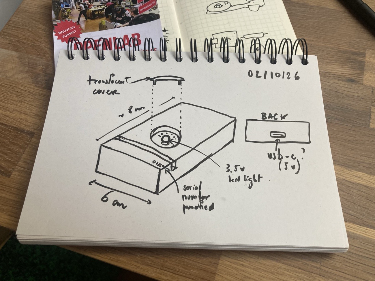 a hand-drawn sketch in a notebook of a wooden stand, about 6 by 8 centimetres, with a 3.5V LED light under a translucent cover, a USB-C socket at the back, and a punched serial number